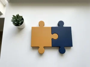 Amber and navy puzzle pieces interlocking on a white desk beside a small green plant, symbolizing Dutch-remote developer collaboration.