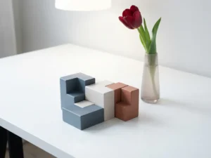 Geometrische bouwblokken in leisteenblauw, gebroken wit en terracotta op wit bureau, naast een enkele tulp in slanke vaas.