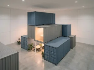 Gestapelde modulaire zeecontainers in geometrische formatie in een minimalistisch kantoor, één container verlicht met warm amber licht.