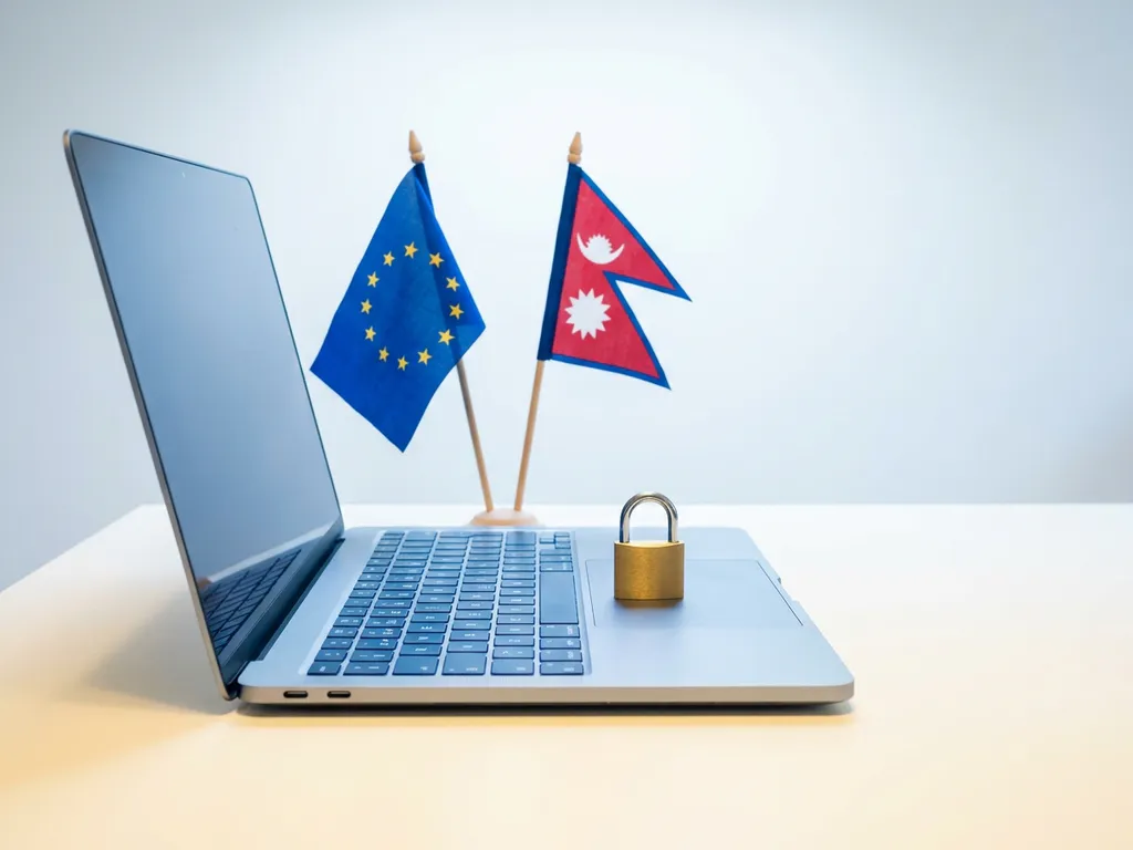 Open laptop on a white desk with EU and Nepalese flags beside a closed padlock symbolizing cross-border data compliance.