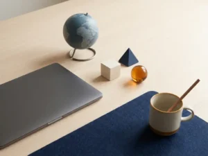 Minimalist desk setup with laptop, small globe, and three geometric connector pieces arranged in a triangle, evoking distributed project team management.
