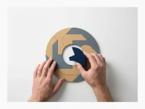 Hands placing the final piece of a geometric puzzle on a white desk, navy and sand tones, flat lay composition suggesting resolution.