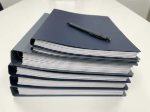 Stack of technical specification documents with precise alignment on a white desk, mechanical pencil resting diagonally across the top page.