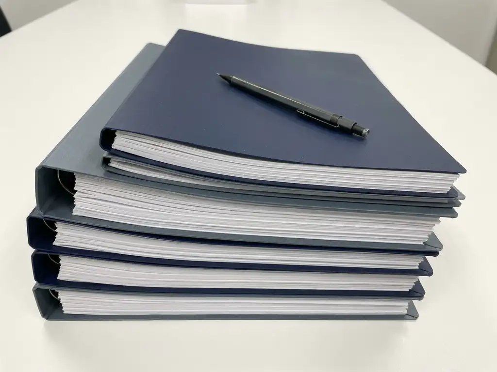 Stack of technical specification documents with precise alignment on a white desk, mechanical pencil resting diagonally across the top page.
