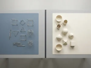 Architectentekentafel van bovenaf met geometrische wireframe modellen in zilver naast gladde keramieken objecten in ivoor.