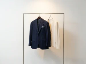 Op maat gemaakt marineblauw colbert naast een confectiepak op minimalistische kledingrek, warm studiolight benadrukt kwaliteitsverschil.