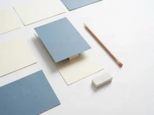Papieren prototype van een mobiele app, opgebouwd uit uitgeknipt karton op een wit bureau met potlood en gum.