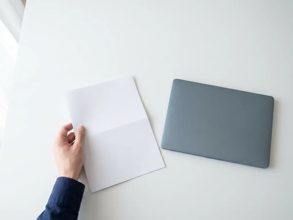 Professional legt een omgekeerde checklist op een wit bureau naast een gesloten laptop in een minimalistische kantooromgeving.