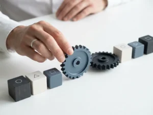 Hand die een stilstaand tandwiel op gang brengt op een wit bureau met geometrische projecttijdlijnmarkeringen in gedempte tinten.